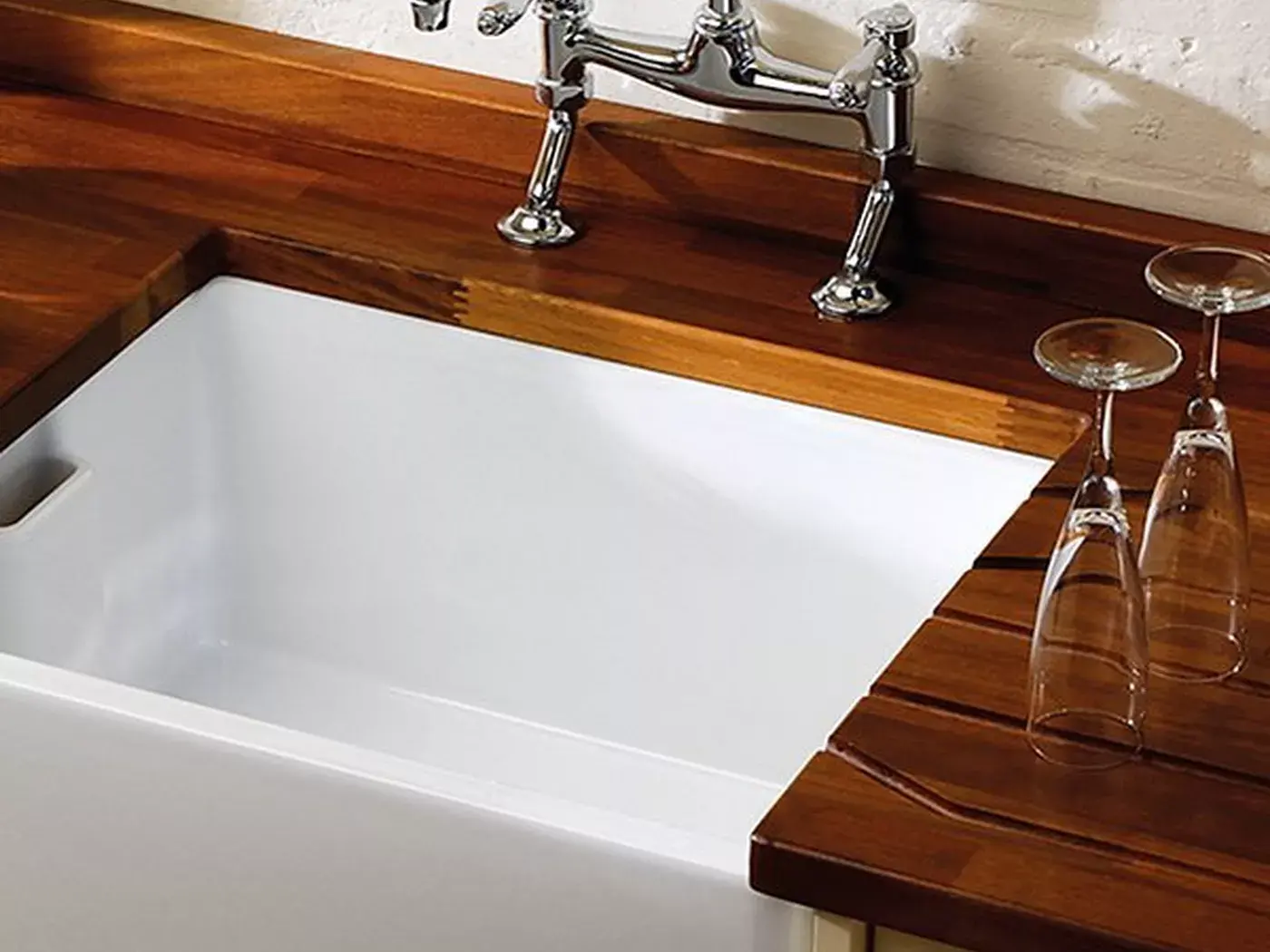 White Belfast sink with a chrome bridge mixer tap set into a timber worktop