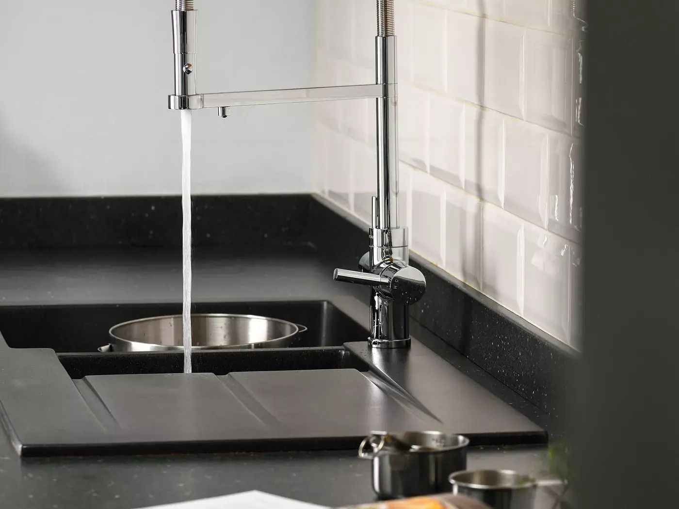Chrome kitchen tap above a dark sink with a white tiled splashback
